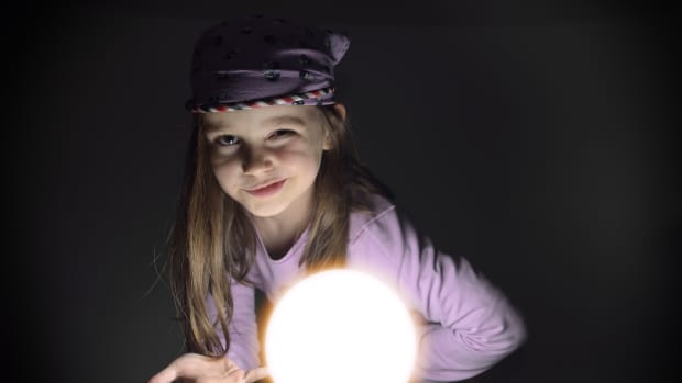 Little girl with bandana winks next to a floating orb of light.