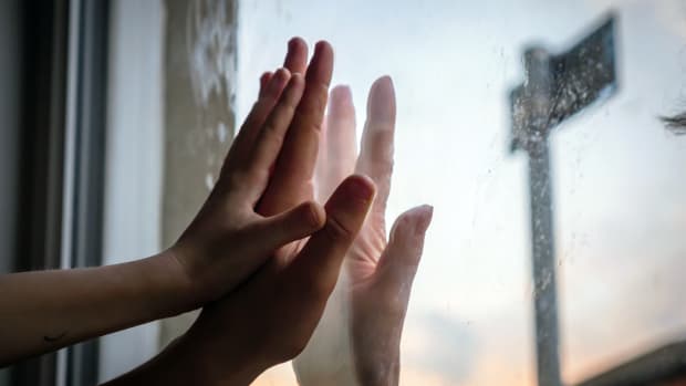 The hands of a mother and daughter press against window glass where the grandmother's ghostly hand appears on the other side.