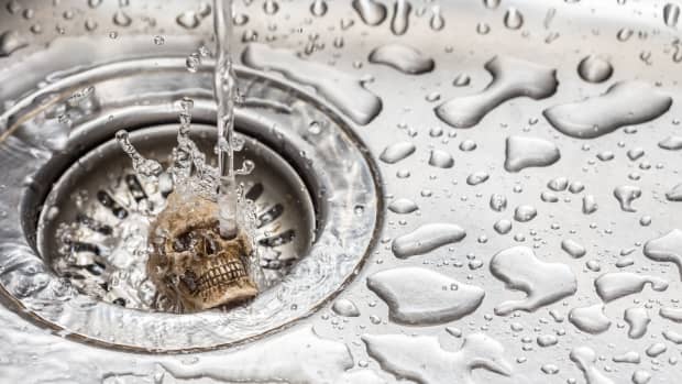 Tiny skull in the drain of a sink with water dripping on it.