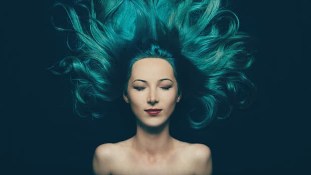 a woman lies down, her eyes closed, her bright turquoise hair spread around her like a halo