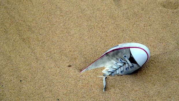 Lost grey and white sneaker, half hidden in sand on a beach with footprints leading away.