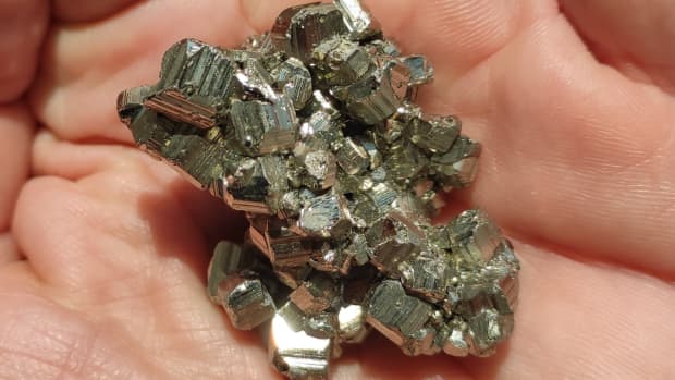 a hand holding a shiny chunk of pyrite