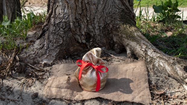 A burlap sack tried with a red bow placed at the foot of a tree.