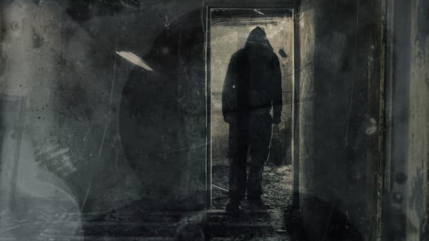 grungy black and white photo of creepy hooded figure standing in doorway of ruined room.