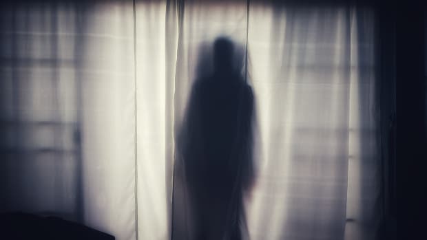 a ghostly silhouette of a man against a backlit curtained window