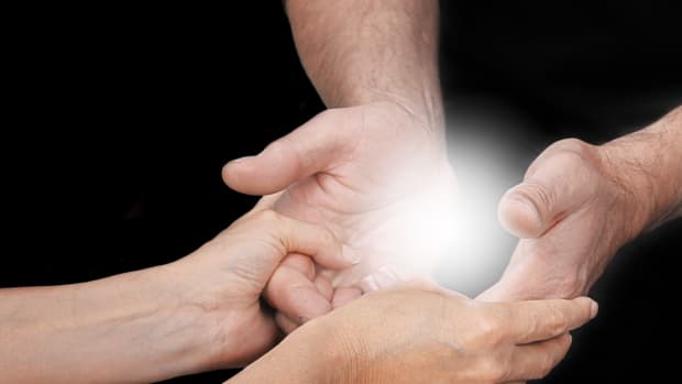 A man and women join their cupped hands. A light shines in the center.