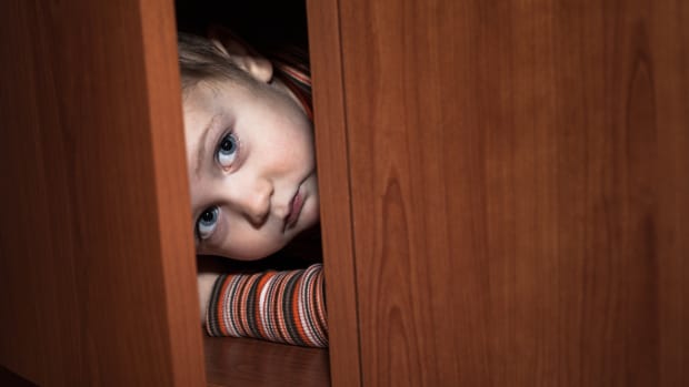 a white toddler boy peeks fearfully out of a partly open cabinet.