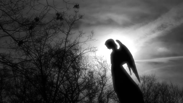 a black and white picture of a silhouette of an angel against a cloudy sky and surrounded by trees.