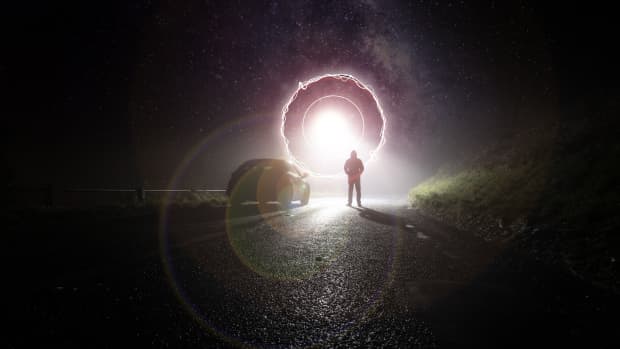 a silhouette of a man on a road with a glowing portal or UFO hanging in the sky