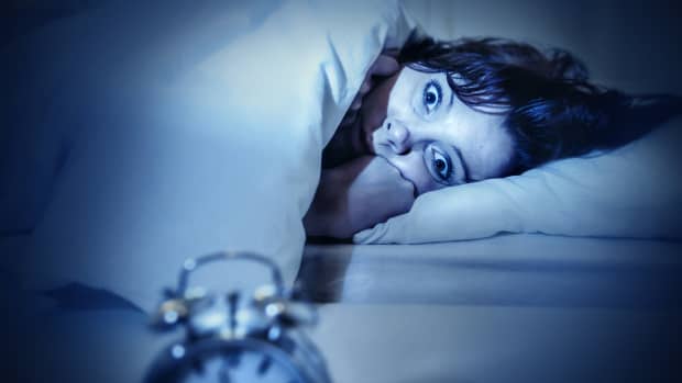 A woman is wide eyed and scared in bed