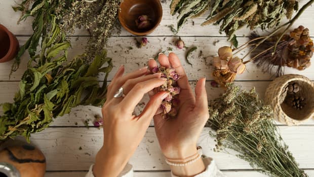 shot from above, a woman's hands working with herbs above a rough-hewn table.
