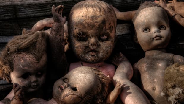 a very creepy, dirty baby doll in a pile with similar dolls