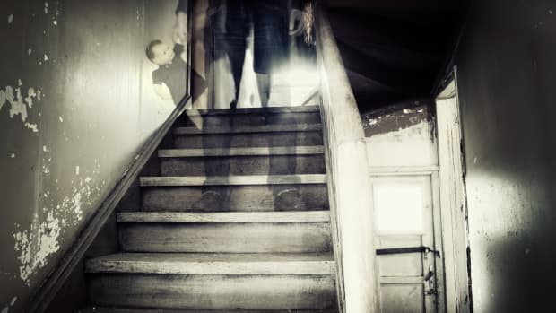 a ghostly figure carrying a babydoll descends a set of creepy stairs in a desaturated photo