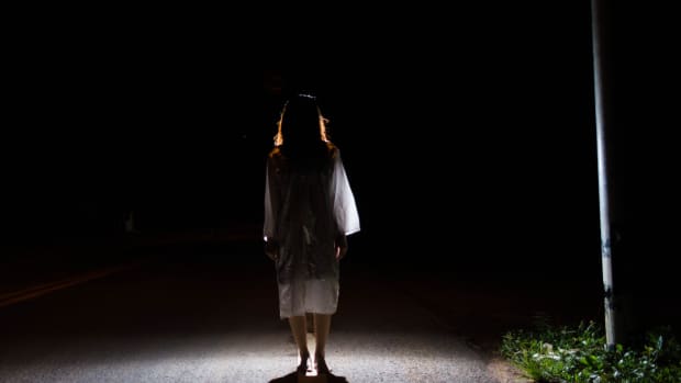 a ghostly female figure stands on a dark, empty road