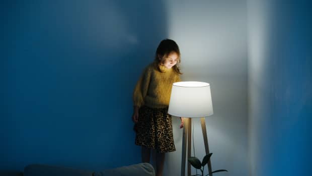 a girl stands on the back of a couch looking into a lamp
