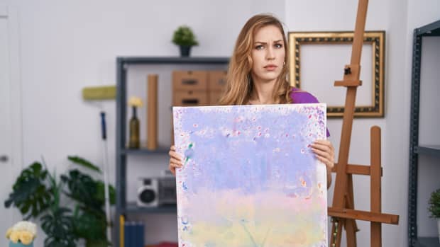woman holds up a painting, looking skeptical