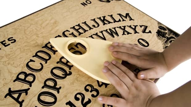 The hands of a small child placed on a Ouija board planchette.