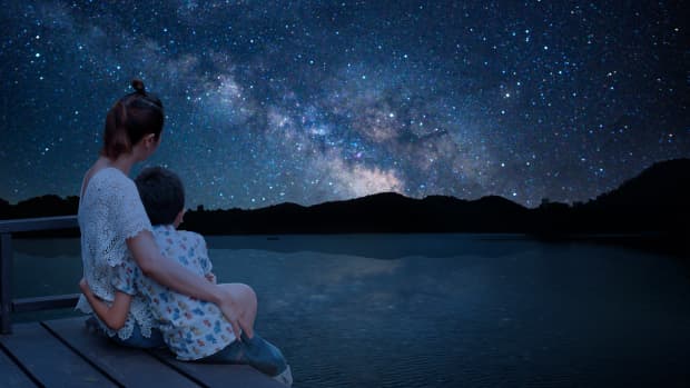 A mother and son cuddle on a dock underneath a brilliant starry sky