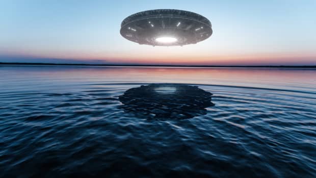 A UFO hovering above a body of water at sunset.