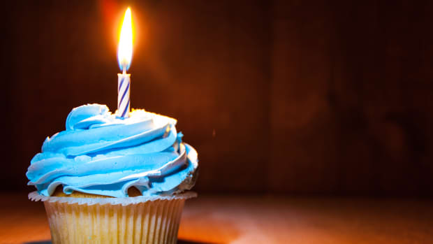 a lit candle on a blue cupcake against a dark background