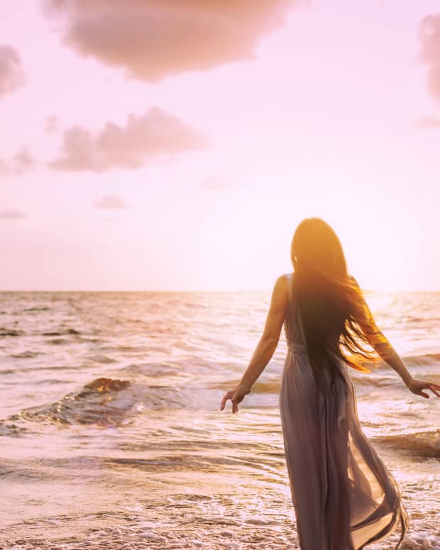 Woman standing with arms spread in front of a shimmer sea at sunrise