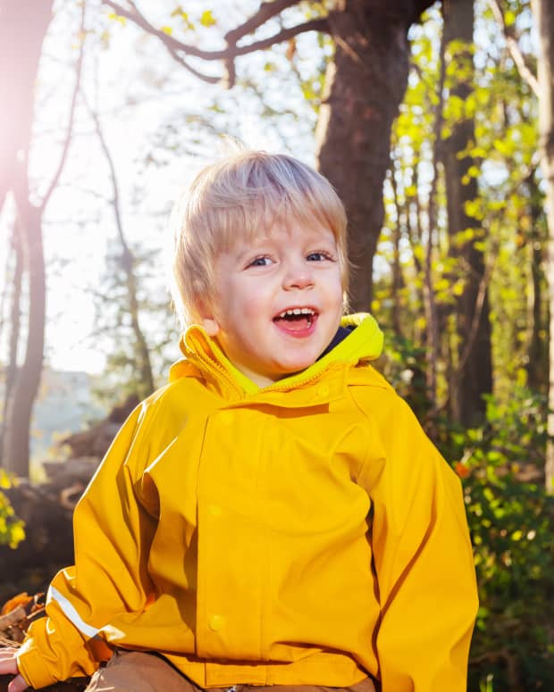 A little boy in a yellow jacket in a sunlit wood