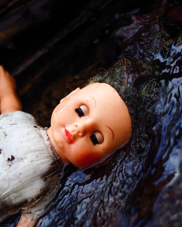 An old plastic doll floats in a stream in the woods