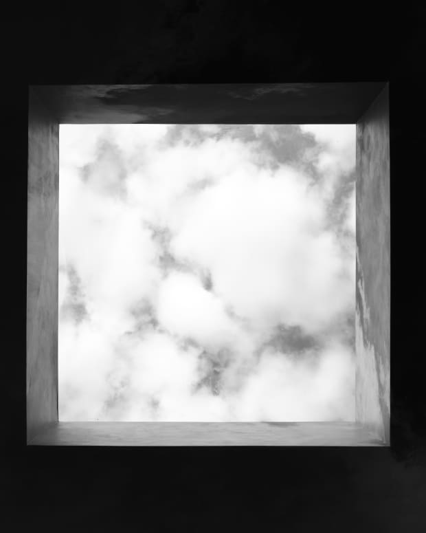 A cloudy sky viewed from below through a square opening in the darkness.