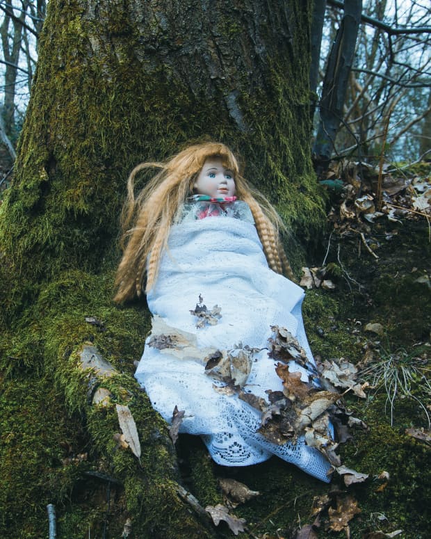 Creepy blonde doll sits under a tree in a silent wood