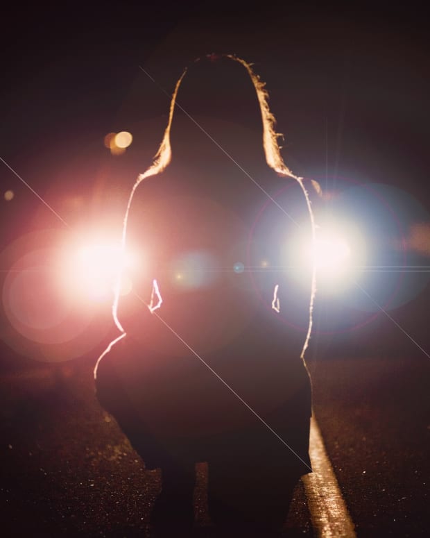 Woman kneeling in the dark in front of a pair of headlights.