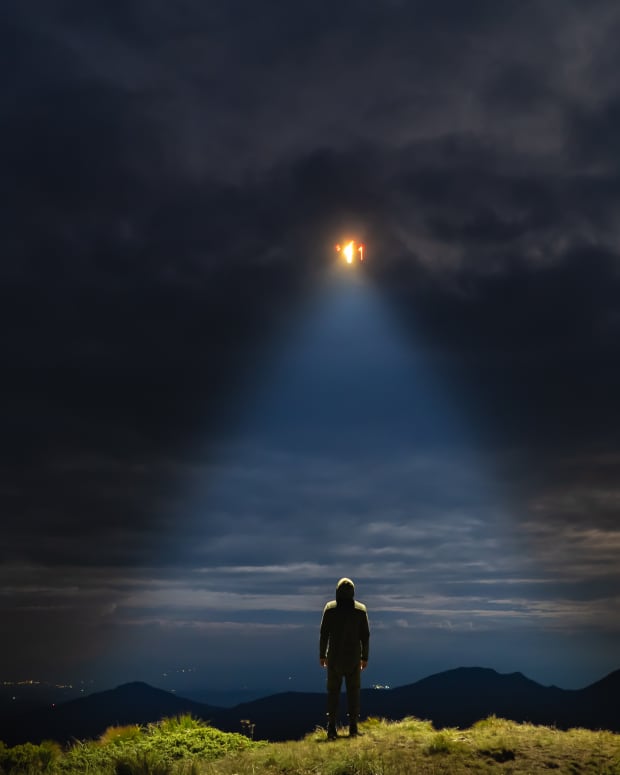 UFO in a cloudy sky shines light down on a man standing on the ground
