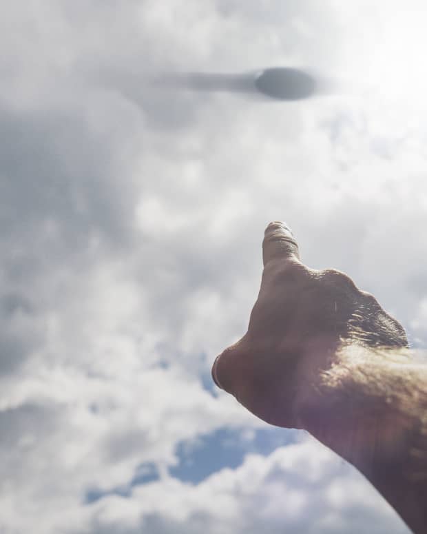 A man's hand points up at a blurry UFO in the sky