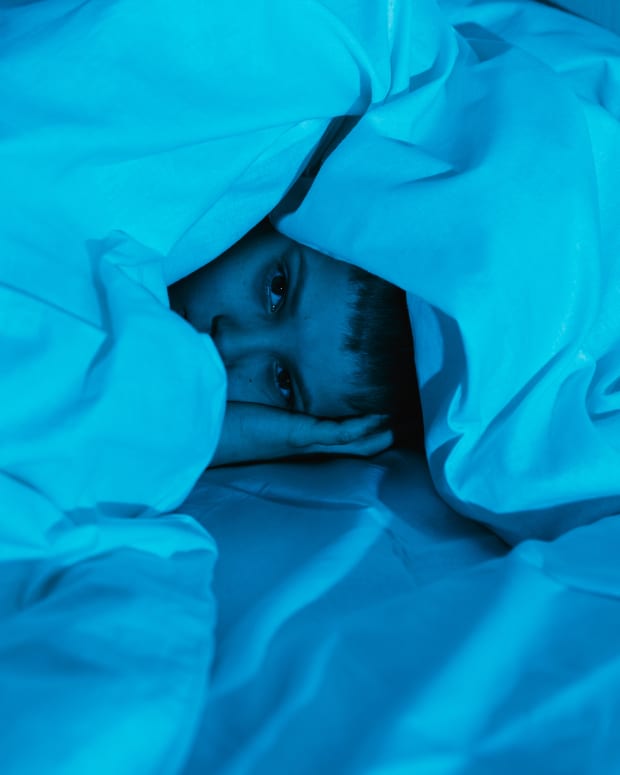 A boy huddles under a mountain of white blankets in soft blue light.