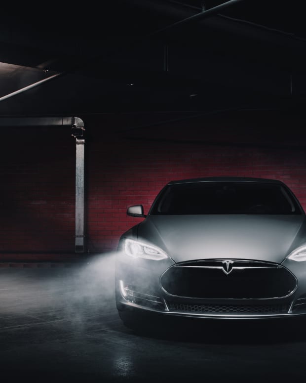 A Tesla in a dark room, its headlights shining on mist