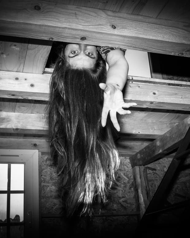 Black and white photo as woman reaches down out of the opening in a ceiling.