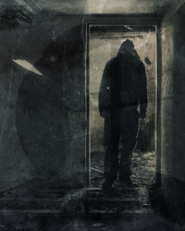 grungy black and white photo of creepy hooded figure standing in doorway of ruined room.
