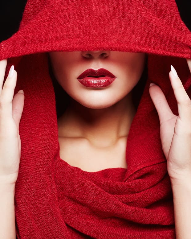 A white woman in a red hooded cloak with bright red lipstick