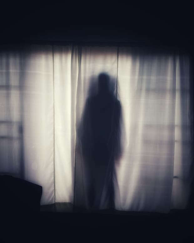 a ghostly silhouette of a man against a backlit curtained window