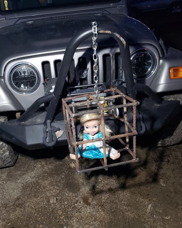 An Elsa doll is trapped in a cage made of rebar on the front of a Jeep