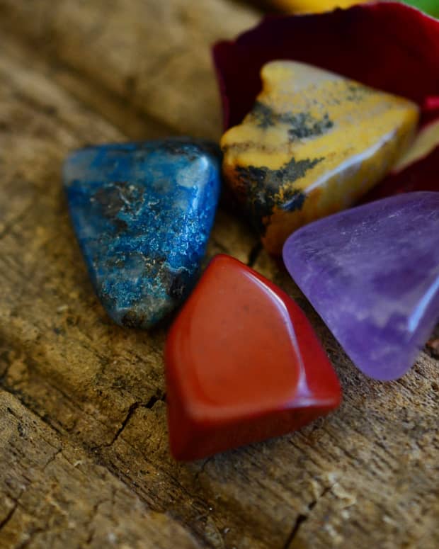 an array of colorful tumbled crystals against a piece of wood.