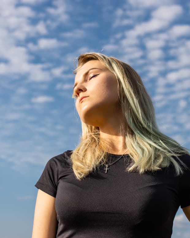 Blond woman, eyes closed, seems to be listening to a sky dotted with clouds.