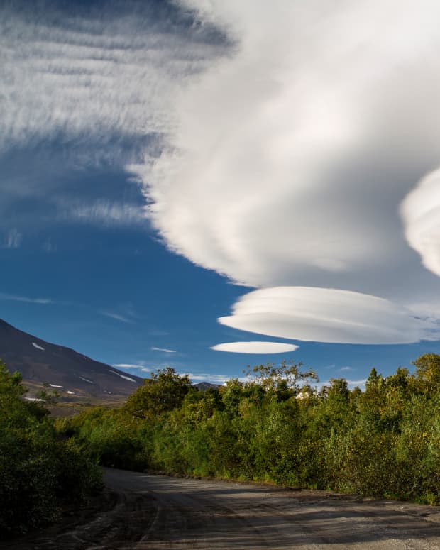 a lenticular cloud resembles a silver flying saucer as it floats above a road