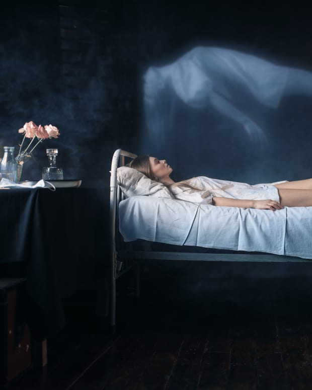 A woman lies in the darkness in a hospital bed, a table with flowers and bottles visible nearby. Her translucent spirit seems to be lifting out of her body.