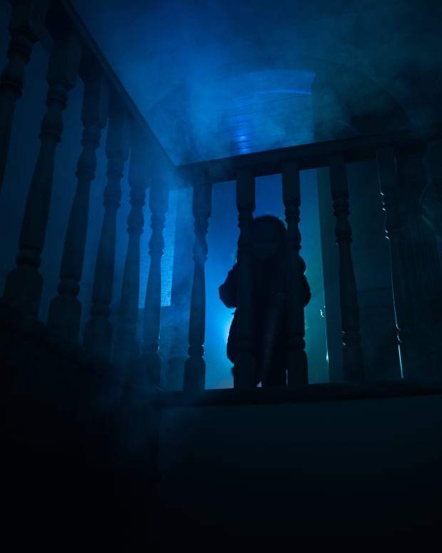 the silhouette of a child looking down through a bannister railing, eerie blue smoke