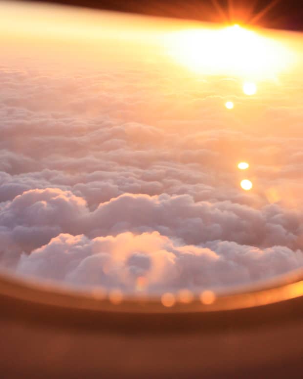a beautiful sunset above the clouds through the window of a plane.