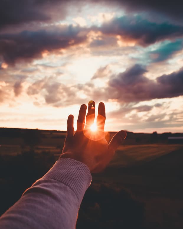 Man holds his hands up to the light shining through his fingers against a beautiful cloudy sky