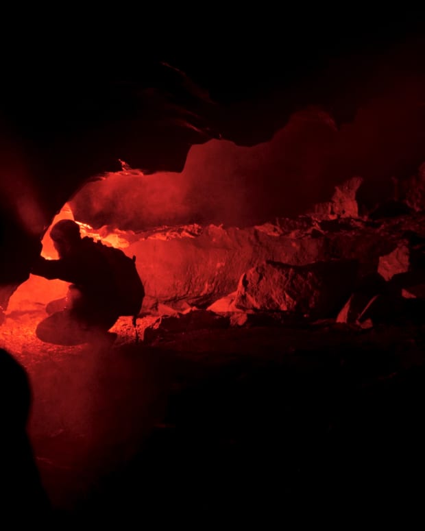 A person kneels in a red-lit cave.