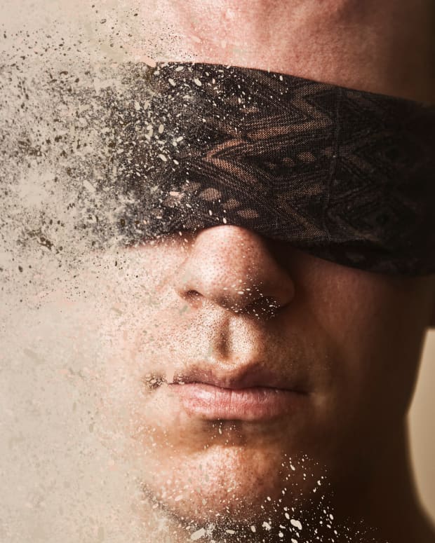 an artistic close up on a blindfolded man's face, dissolving into dust