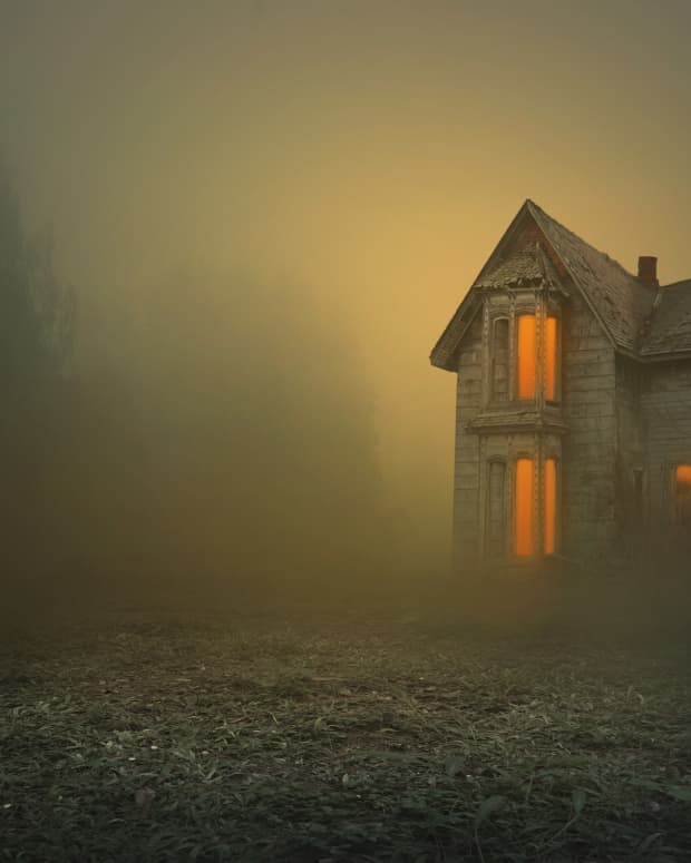 lights glow from the windows of a creepy old house in a mustardy mist
