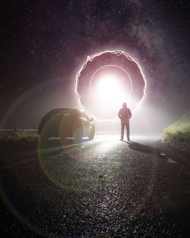 a silhouette of a man on a road with a glowing portal or UFO hanging in the sky